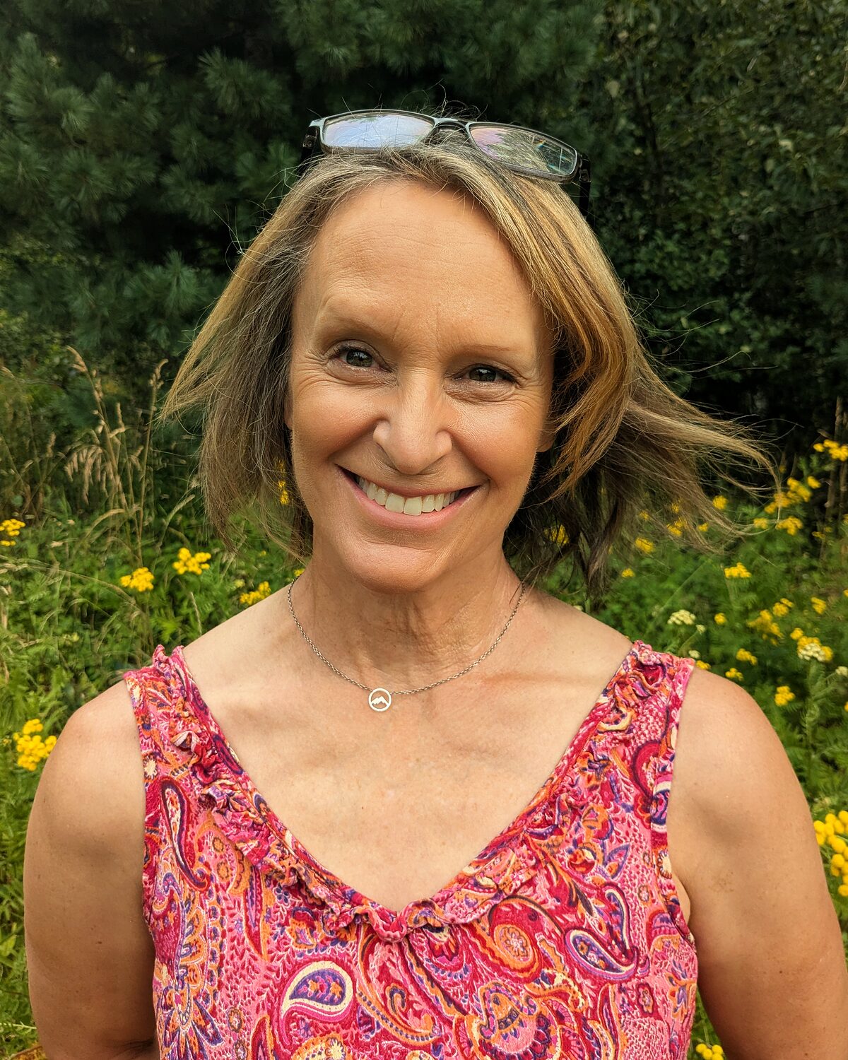Anne Marie Norling outdoors, smiling, with summer foliage behind her